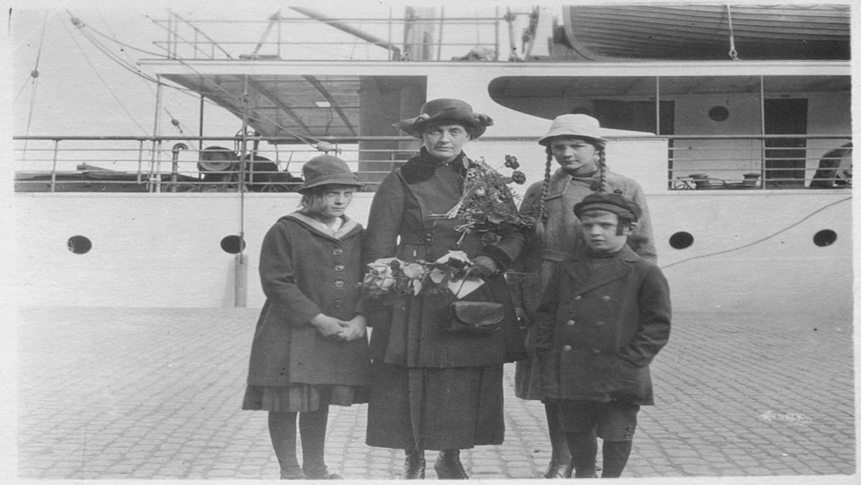 Nainen ja kolme lasta laiturissa olevan laivan edustalla.