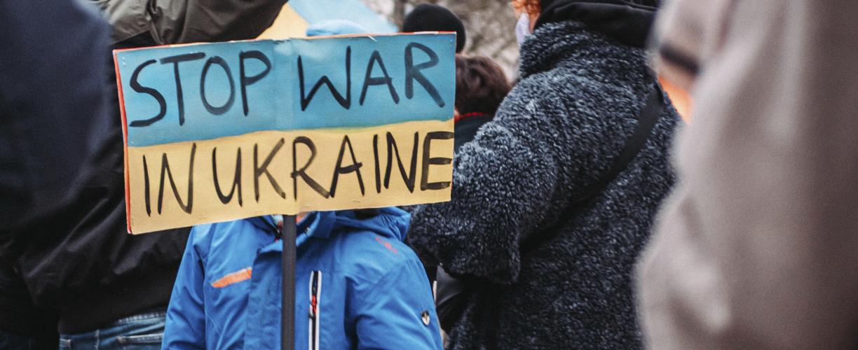 Ihmisiä mielenosoituksessa. Väkijoukon keskellä sinitakkinen henkilö pitää kylttiä, jossa lukee "Stop war in Ukraine".