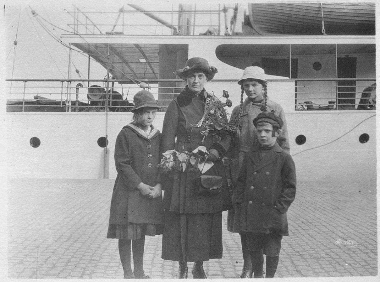Nainen ja kolme lasta laiturissa olevan laivan edustalla.