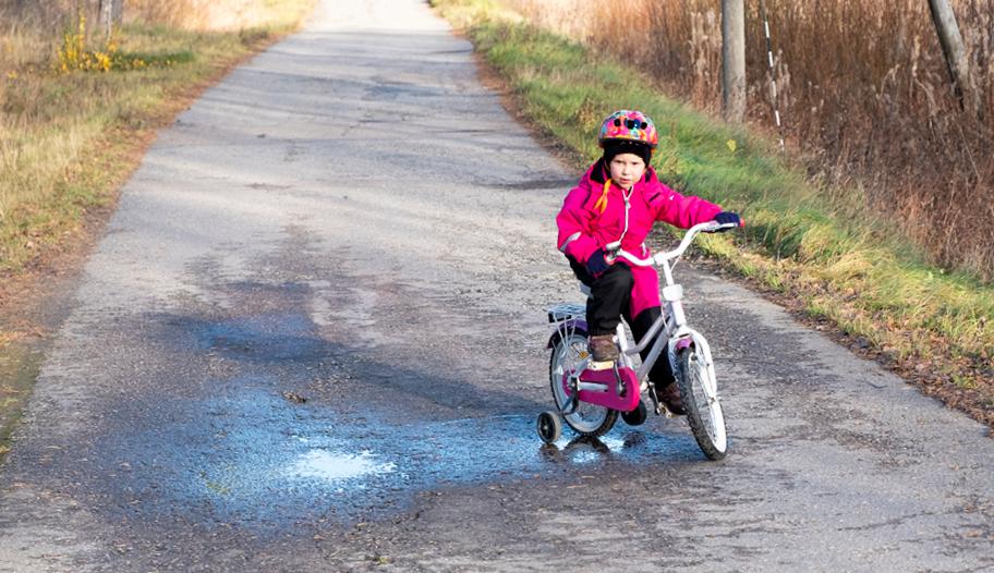 Lapsi ajelee syksyisessä maisemassa polkupyörällä, jossa on apupyörät.